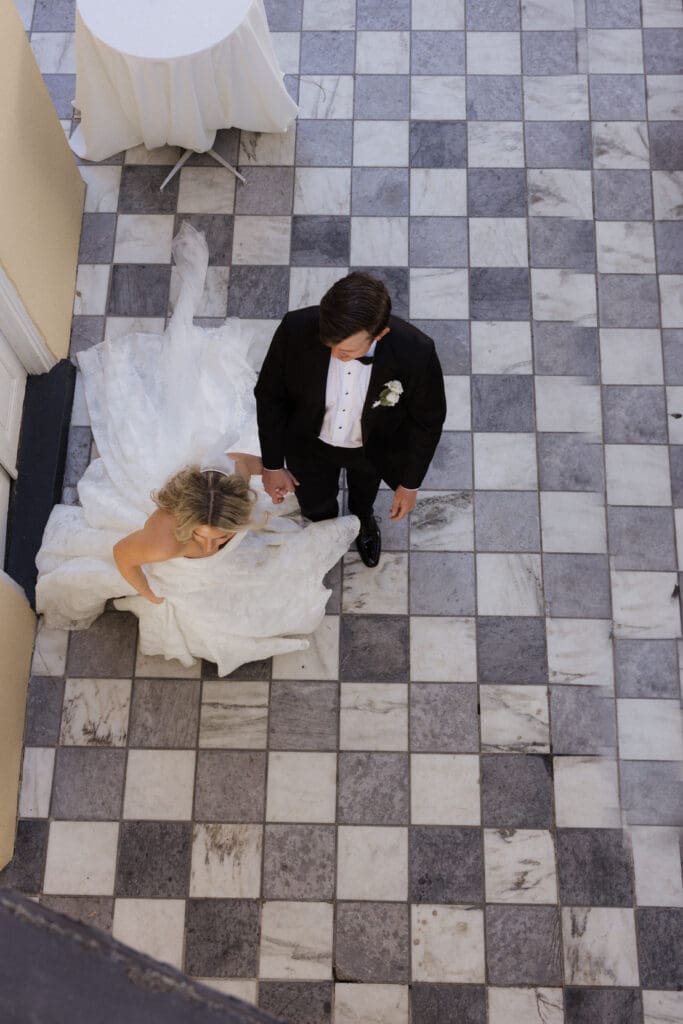 Aerial view of a couple just getting married and holding hand in gown and tux. Checked floor in the background