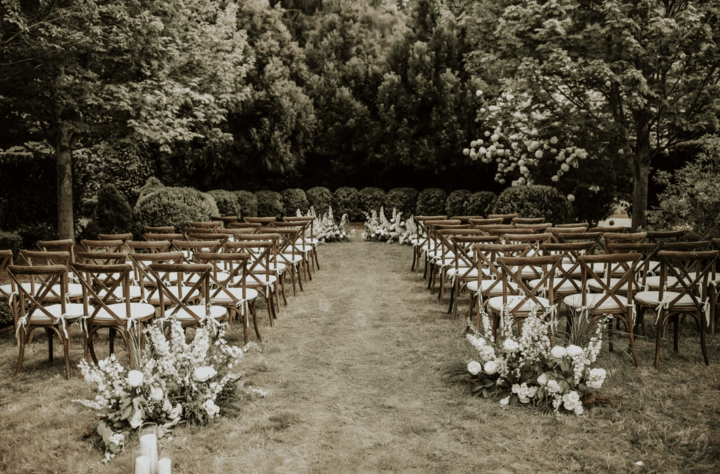 The Andrew Farm is surrounded by lush green trees with white rows of flowers lining the walkways of chairs for guest to witness a beautiful wedding.