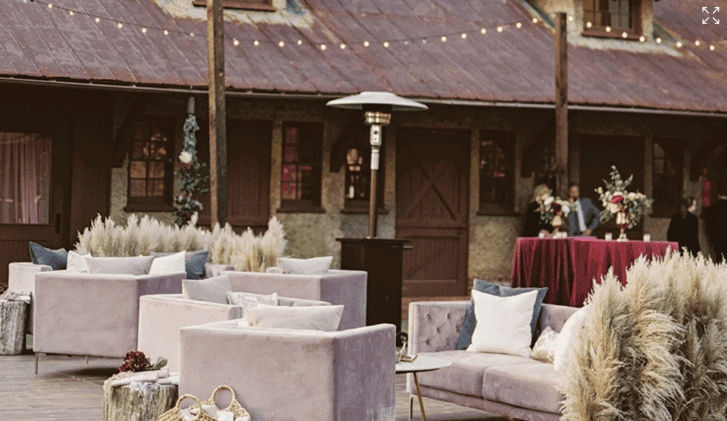 Patio of the Biltmore with blush color sofas and chairs with string lights and a rustic appearance of the roof line of the barn. 