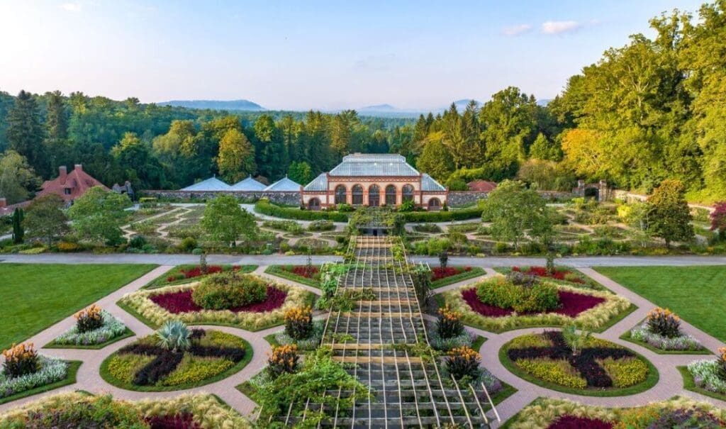 The Biltmore manicured gardens with greens and red color plants that are planted in circular and linear stone pathways. The pathways lead up to the front of the estate.