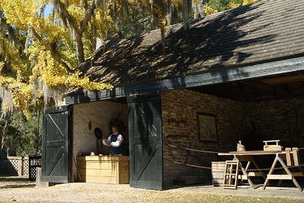 Middleton Place Museum a man re-enactment of life ages ago in a barn type farmhouse dressed in period clothing. The other area in the barn has a sawhorse and has carpenter tools