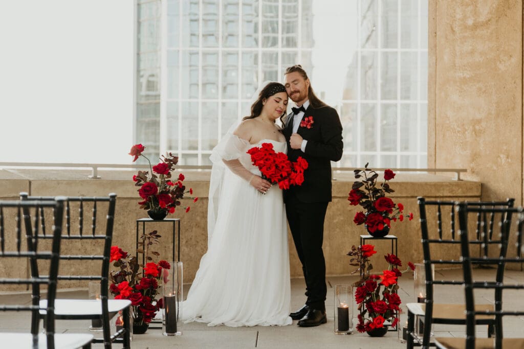 Couple posing for a wedding photo in the Mint Museum in Charlotte North  Carolina Wedding Venue with red roses surrounding them.