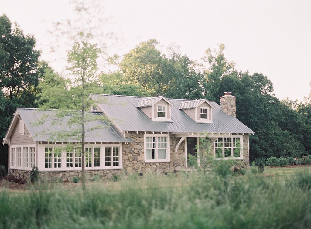 The facade of Morning Glory Farm Venue has a rustic stone front surrounded by oak trees and open fields,