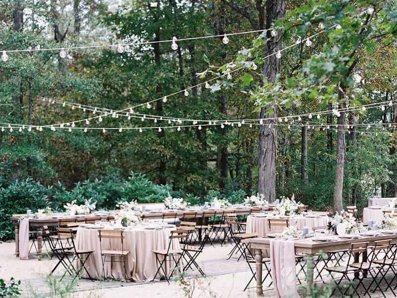 Morning Glory Farm reception area with table linens and flowers with string lights surrounded by lush greenery and trees on the veranda.