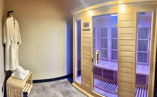 Urban Wellness Center spa interior with a dry sauna and purple lighting with robes and towels sitting on a crate outside the sauna.